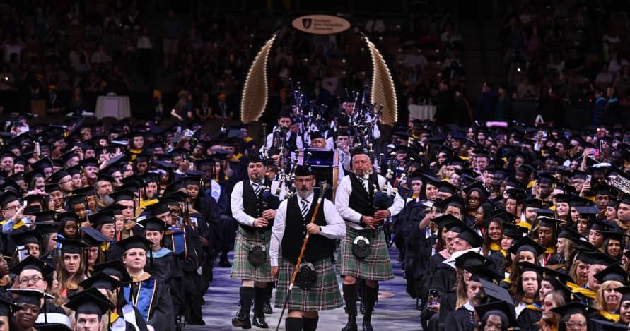 Rows of graduating students as a procession of bagpipers go down center aisle during Fall commencement ceremony.