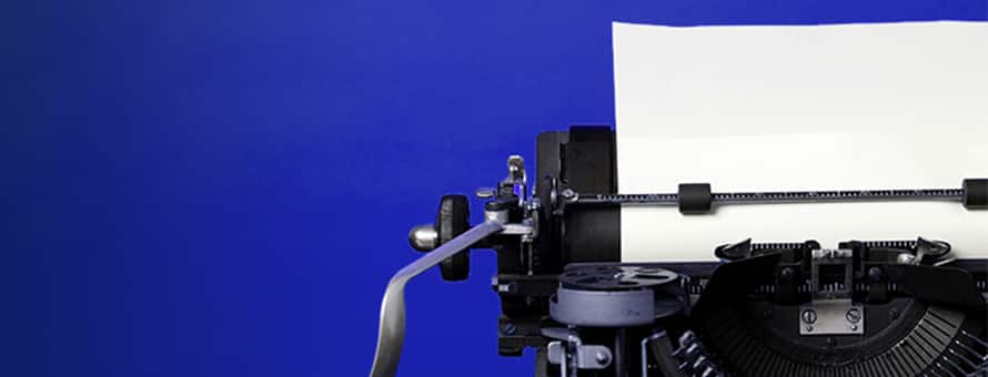 The upper left corner of an old fashioned typewriter with a blank sheet of paper loaded and clipped in place.