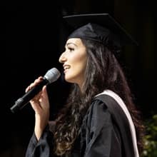Fatma Salem Pease in her cap and gown holding a microphone and singing the national anthem at SNHU's 2019 Commencement.