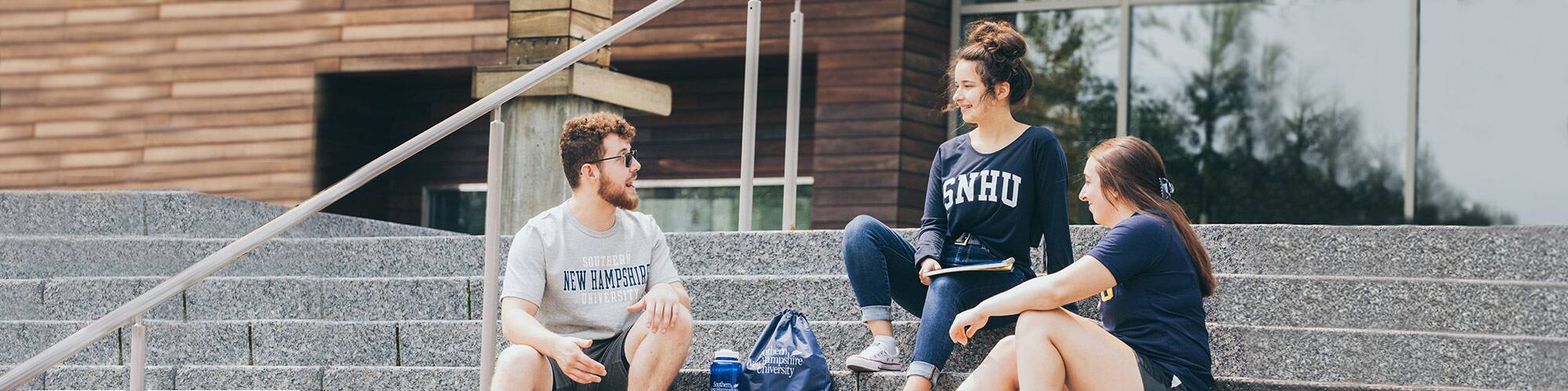 Three students sitting and talking on the library steps on SNHU campus