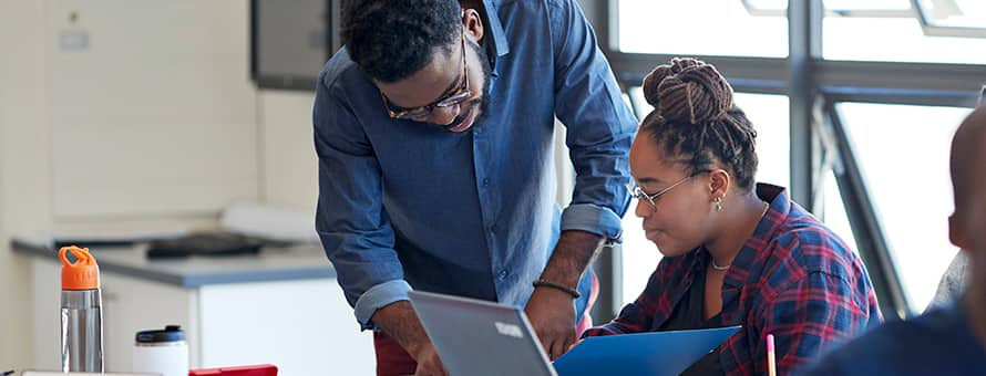 An educator exhibiting the qualities of a good leader while he helps a student on her laptop.