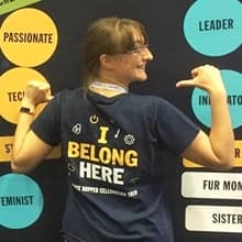 A woman at the Grace Hopper Celebration pointing with her thumbs to the back of her T-shirt that reads I Belong Here.