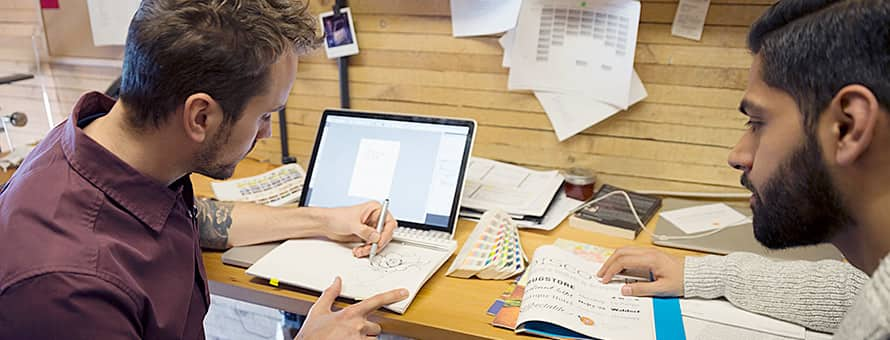 Two men sit at a table and discuss how to create a graphic design portfolio