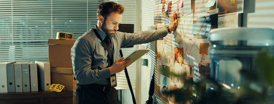A detective with a criminal justice degree, leaning against a map and reviewing a case file in his hand.