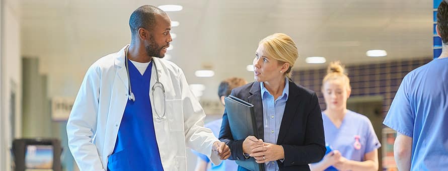 A healthcare administrator speaking with a doctor as they walk down a hospital hallway.