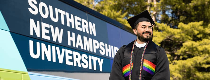 Jesús Suárez wearing his cap and gown in front of the Southern New Hampshire University bus