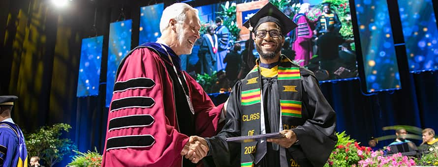 Matthew Seawright a 2019 bachelors in business administration graduate from SNHU shaking hands with SNHU president Paul LeBlanc as he gets his degree