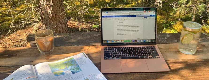 A laptop, textbook and two drinks resting on a makeshift outdoor desk.