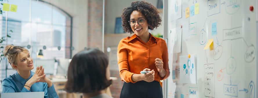 A marketing manager presenting ideas on a whiteboard during a team meeting while colleagues listen.