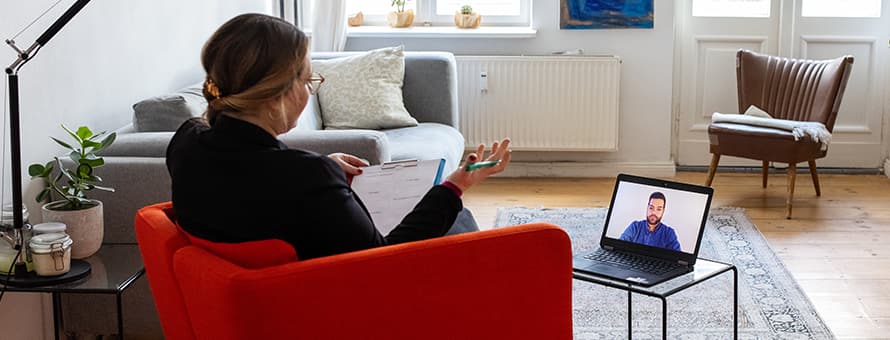 An online therapist taking notes on a clipboard while on a video call with a client.
