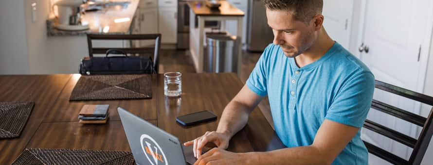 A man sits at a table with his laptop researching how to transfer colleges