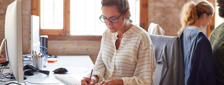 A copywriter writing in a notebook at her desk at a marketing agency.