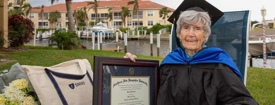 Joan Donovan dressed in graduation cap and gown, holding her SNHU diploma outside of her Florida home.