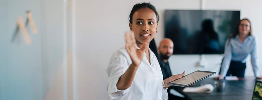 A professional at a white board, presenting the different jobs for master's in communication graduates to a man and a woman in a conference room.