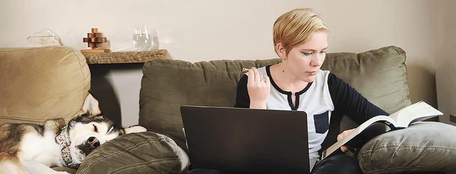 Jolene Stetz studying a textbook with a laptop in front of her and dog asleep beside her.