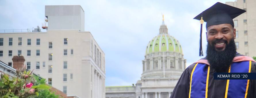 Kemar Reid, 2020 graduate of the online Master's in Public Health program, standing in front of a government building in his graduation cap and gown.