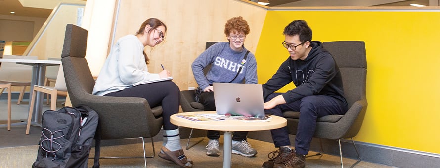 Three college students looking at a laptop while they study for a liberal arts degree