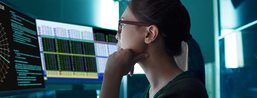 A market research analyst doing her job, reviewing data on three computer monitors.