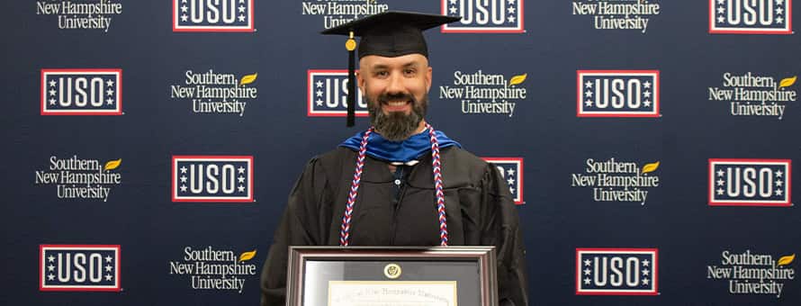 Nathaniel Lohn holding his diploma in front of USO and SNHU sign