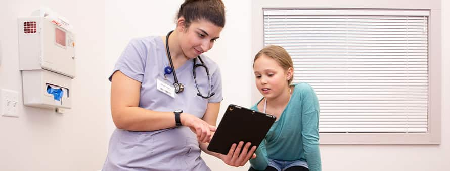 A family nurse practitioner explaining something with a tablet to her patient, a child.