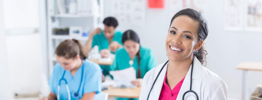 A nurse wearing a lab coat and stethoscope in a classroom with nursing students behind her with words nurse educator career.