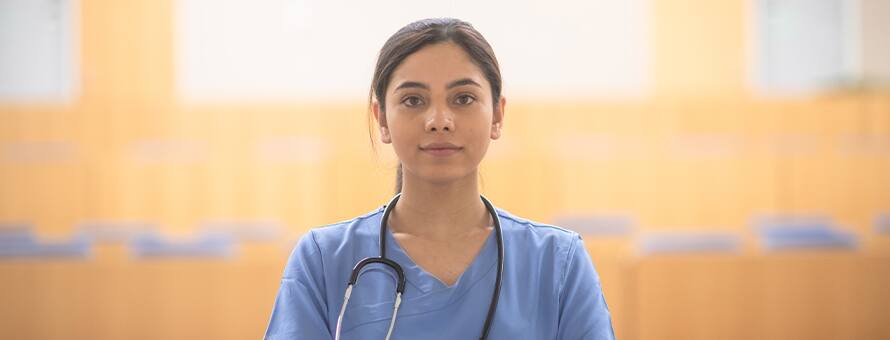 A nurse standing alone during a nursing shortage, wearing scrubs and a stethoscope.