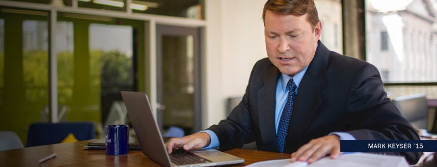 Mark Keyser working on his laptop while looking at papers with text Mark Keyser '15