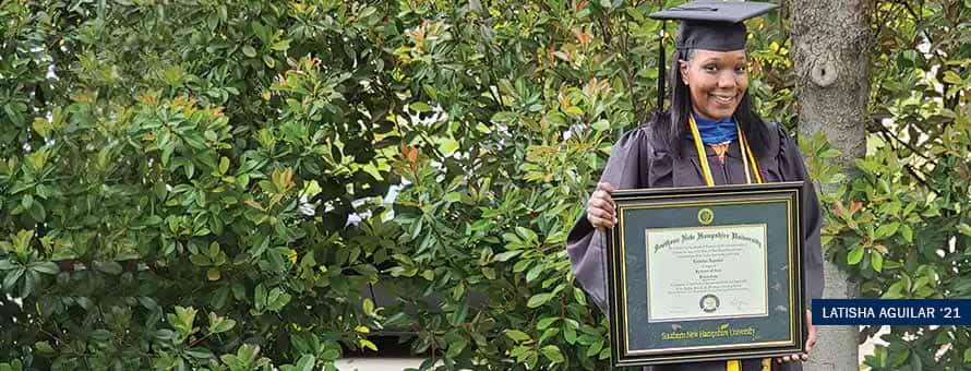 SNHU online college graduate Latisha Anguilar holding up a framed degree in front of the woods
