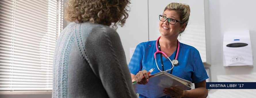 Kristina Libby, an online BSN student, talking to a patient in blue scrubs with black glasses and a pink stethoscope.
