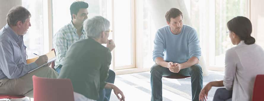 A psychologist and group of clients sitting in a circle during a group therapy session.
