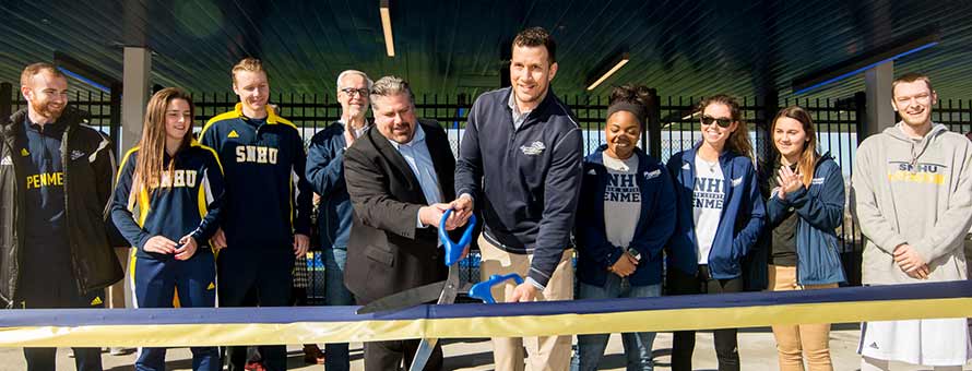 SNHU officials cut a ribbon with big scissors to officially open Penmen Stadium