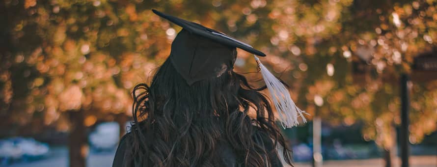 A student wearing a cap and gown walking away from the camera
