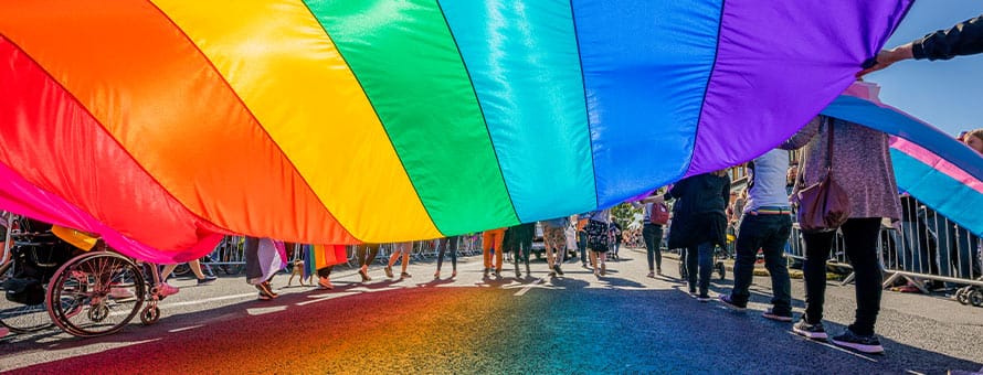 People holding a large pride flag while walking in a pride parade