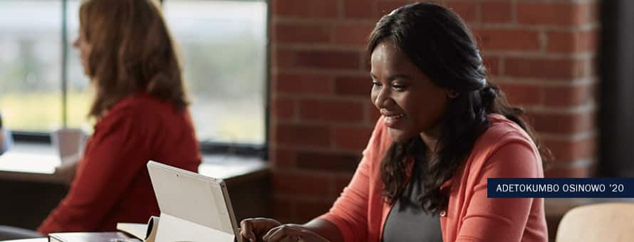 2020 BS in Business online HR degree concentration alumna Adetokunbo Osinowo, working at a laptop in an office setting