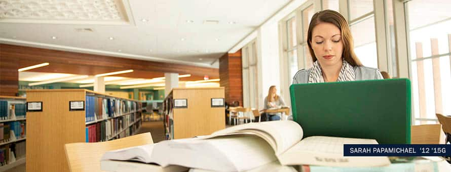 BA History graduate, Sarah Papamichael, working on her laptop in a library. With the text Sarah Papamichael '12 '15G