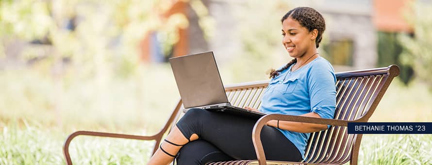 Bethanie Thomas, online bachelor's in geosciences student and future graduate of the 2023 class, using her laptop on a park bench.