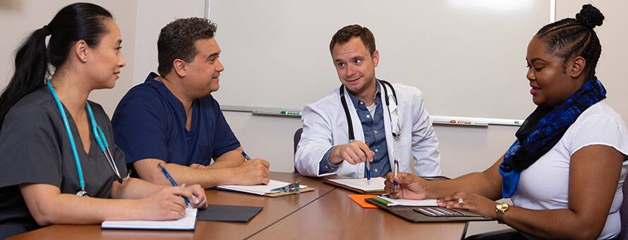 Four medical professionals sitting around a table, discussing quality improvement in healthcare