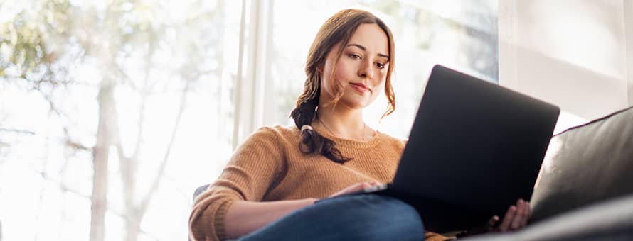 A woman sitting on her couch working on her MA degree on her laptop
