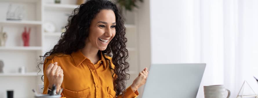 A woman smiling while celebrating a small win at her laptop.