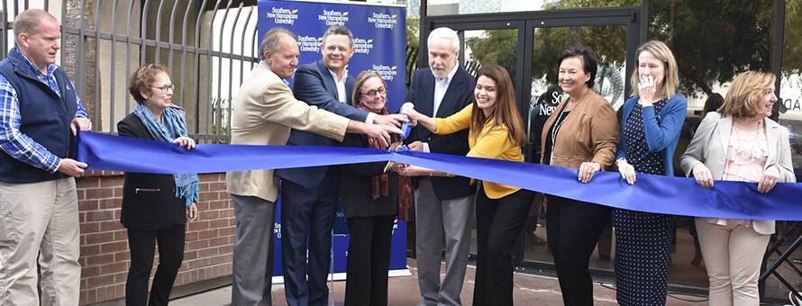 SNHU officials using huge scissors to cut a blue ribbon at the university's new southwest operations center in Tucson, Arizona.