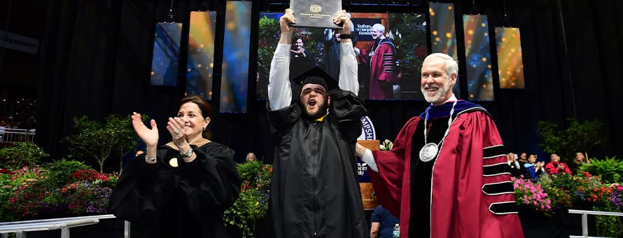 SNHU President Paul LeBlanc (right) and Board of Trustees member Lisa Guertin (left) at commencement with a graduating student (middle) who is holding up his dimploma