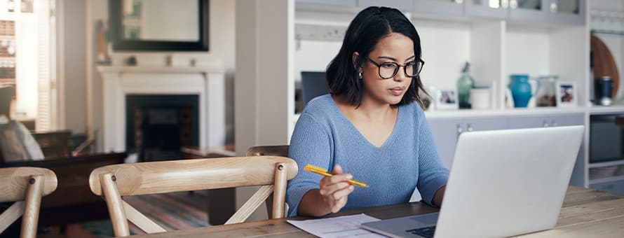 A professional woman holding a pencil and looking at a laptop as she studies for a continuing education certification.