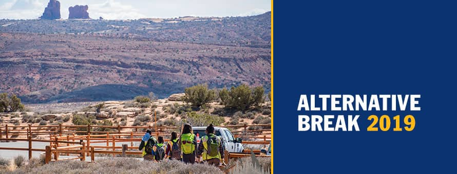 Women in yellow safety vests near a wooden railing in the Utah desert and the text Alternative Break 2019.