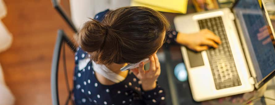 An female online student working on her laptop and talking on a cell phone as part of her virtual internship.