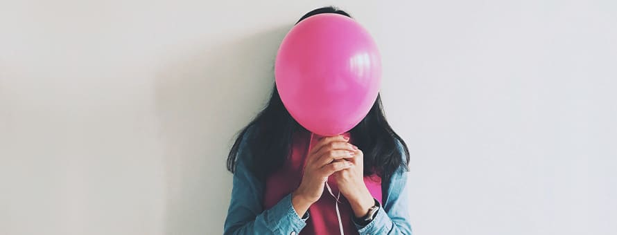 A woman holding pink balloon in front of her face.