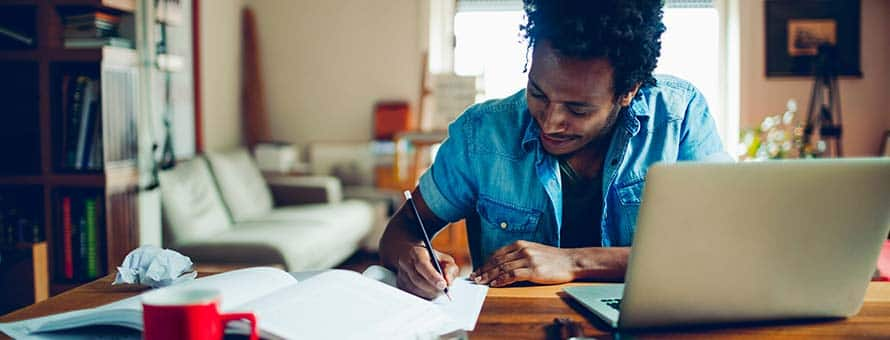 A man working at his desk at home researching how to become a writer.