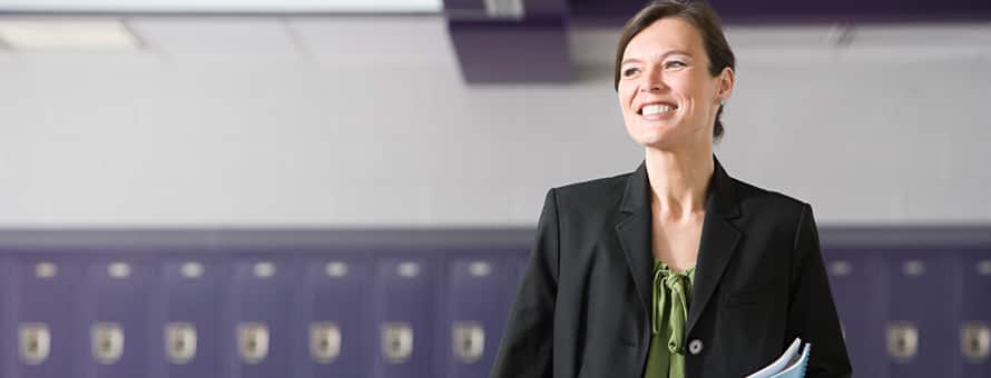 An educator considering the benefits of earning a master’s in curriculum and instruction, standing in front of a row of lockers.