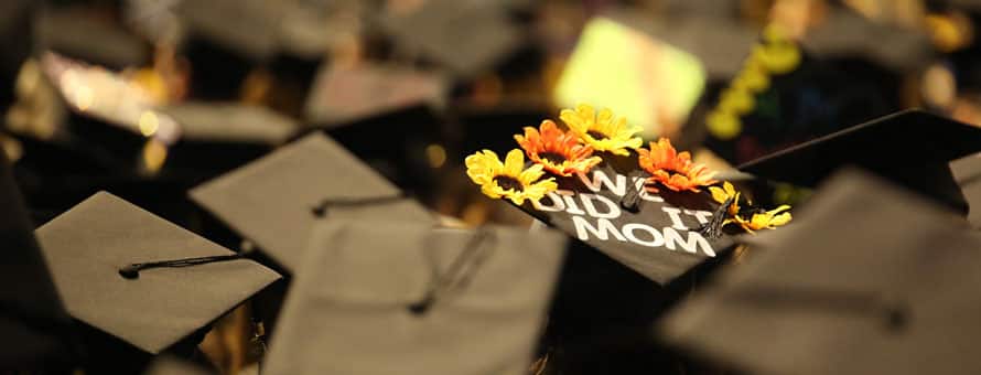 The top of a graduation cap decorated with yellow and orange flowers and the words We did it, mom.