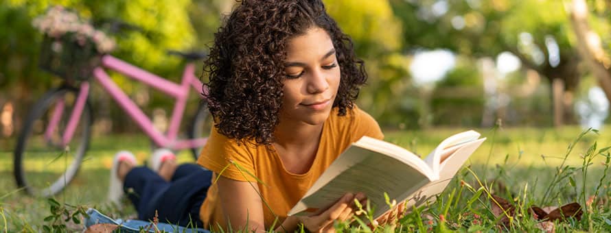 A person laying in the grass and reading a book.