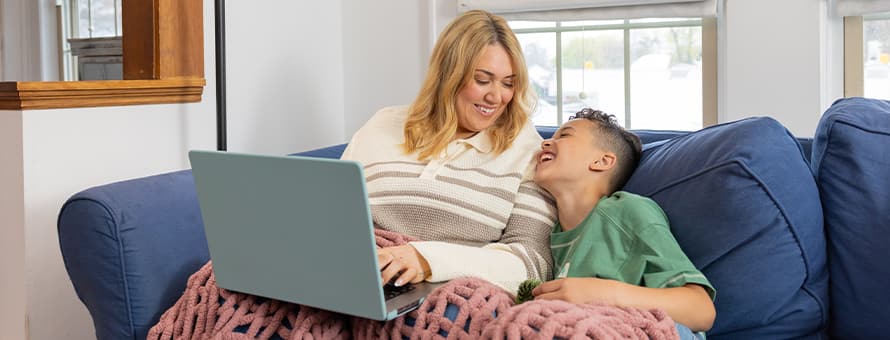 SNHU graduate Madison Richards and her son Malakai sitting on a couch while she works on a laptop, completing her online degree program.